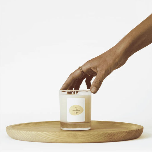 Velas Aromaticas Personalizadas, recipiente de cristal de alta calidad, en transparente, hecha de cera natural 100% y un peso de 180g.
Una mano coge la vela por la parte superior.
