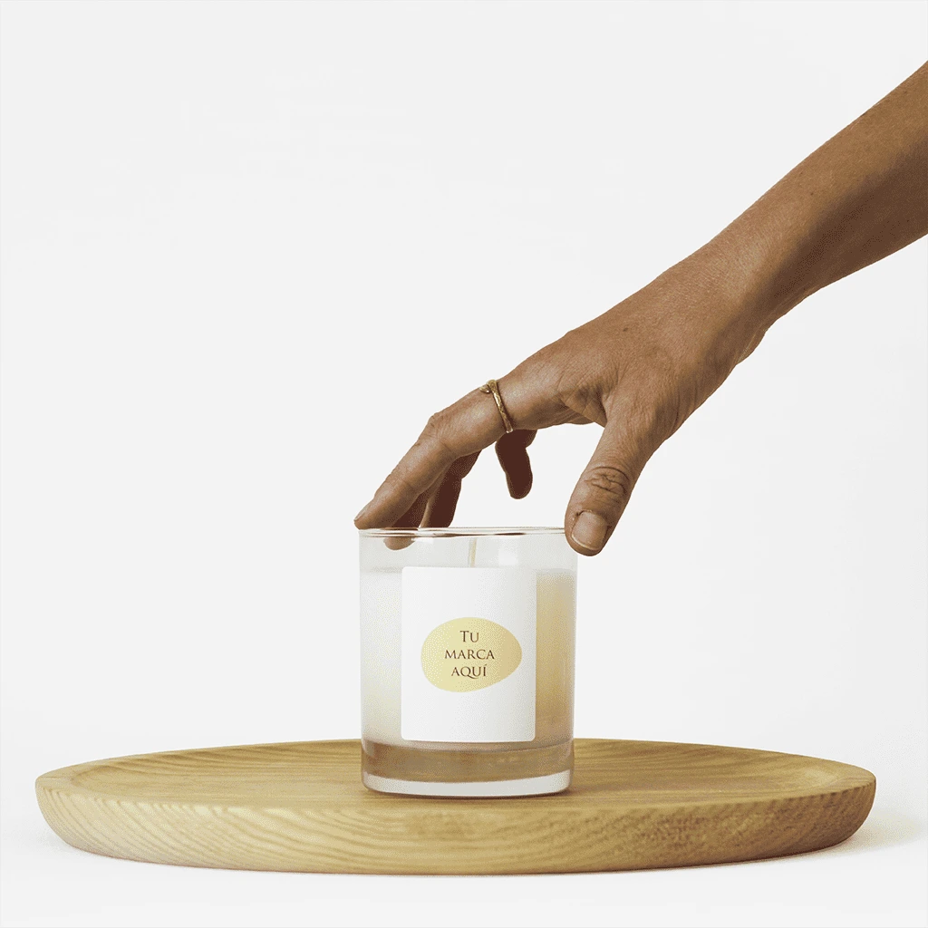 Velas Aromaticas Personalizadas, recipiente de cristal de alta calidad, en transparente, hecha de cera natural 100% y un peso de 280g.
Una mano coge la vela por la parte superior.