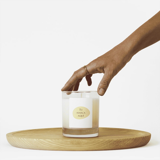Velas Aromaticas Personalizadas, recipiente de cristal de alta calidad, en transparente, hecha de cera natural 100% y un peso de 280g.
Una mano coge la vela por la parte superior.