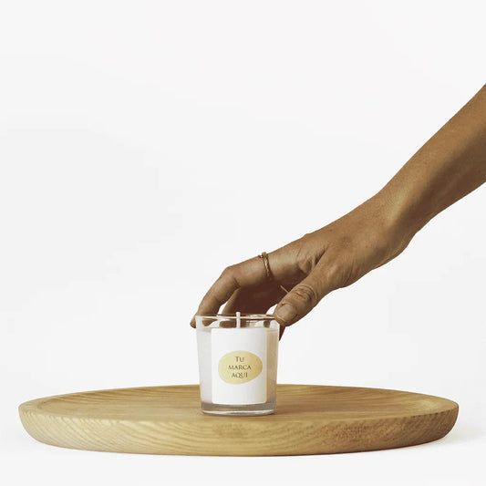 Velas Aromaticas Personalizadas, recipiente de cristal de alta calidad, en transparente, hecha de cera natural 100% y un peso de 80g.
Una mano coge la vela por la parte superior.